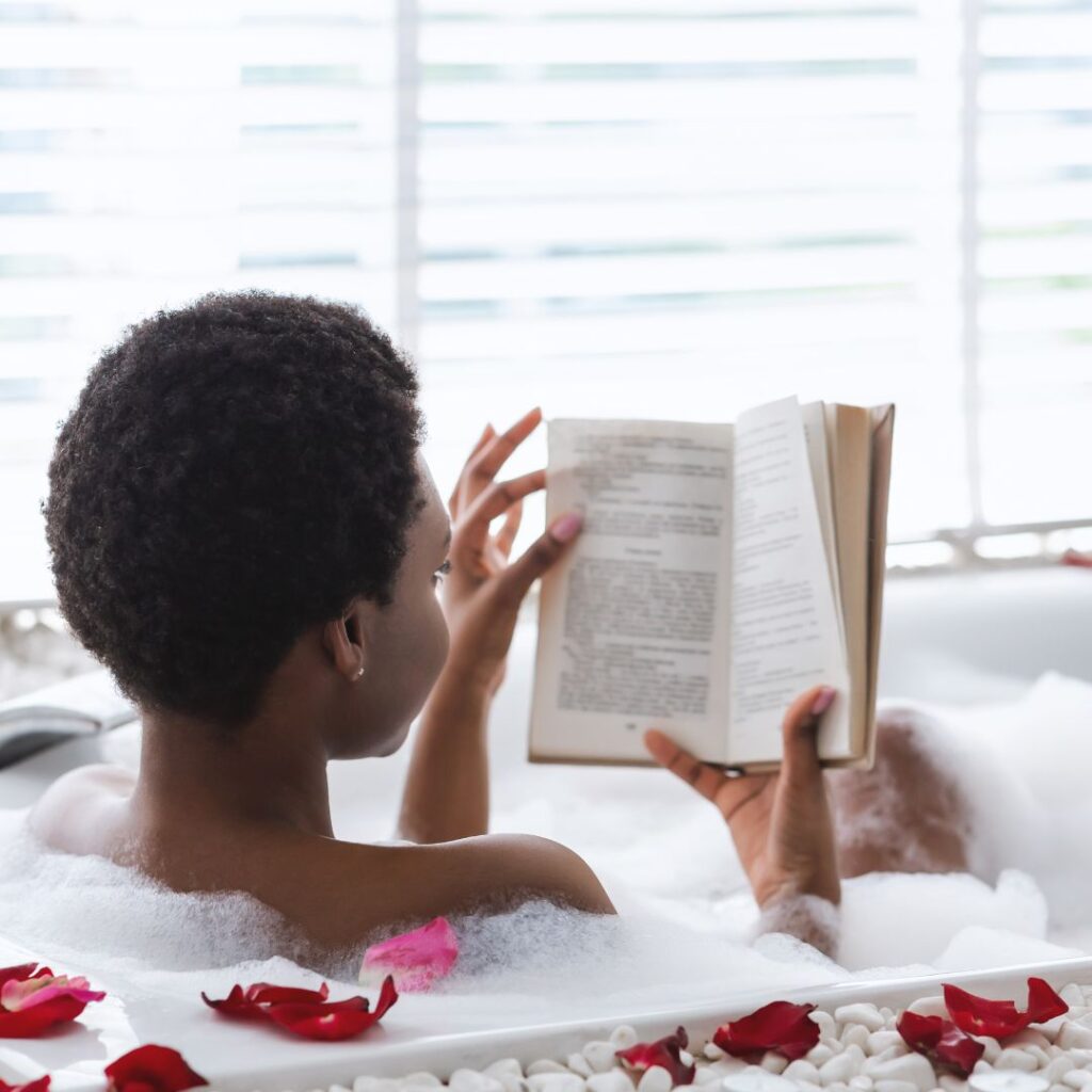 Black of woman reading in a bubble bath for black self-care.