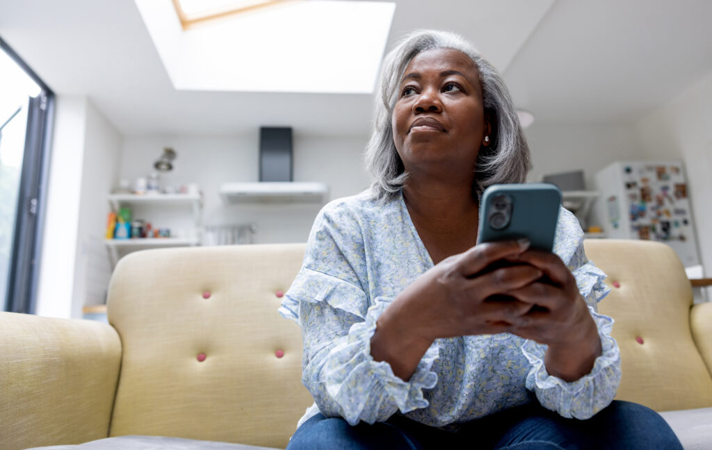 Mature black woman at home texting on her cell phone while sitting on the couch - lifestyle concepts